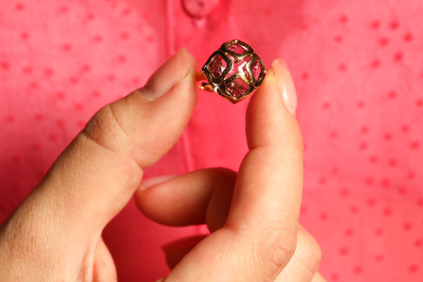 Gold ring with red gemstone held between fingers against a pink polka dot background