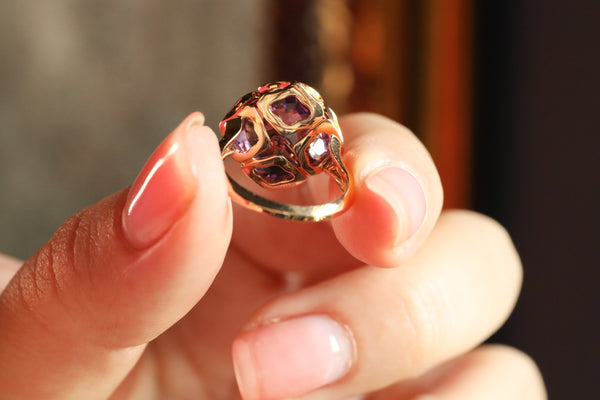 Rose gold ring with gemstones held between fingers against a blurred background