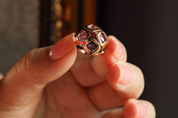 Gold ring with gemstones held in a hand against a blurred background
