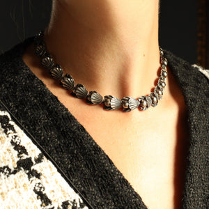 Necklace worn by a person with a patterned cardigan against a dark background