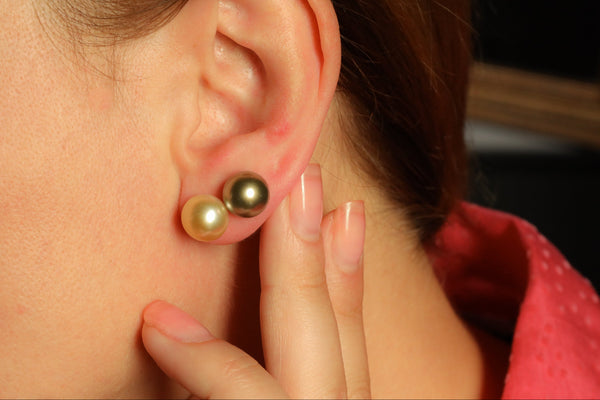 Close-up of an ear with two pearl earrings, one gold and one black, against a blurred background.