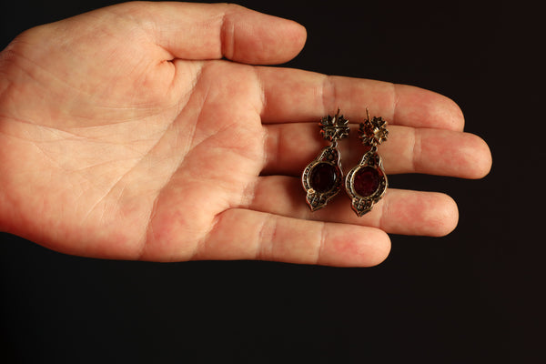 Pair of earrings held in a hand against a dark background