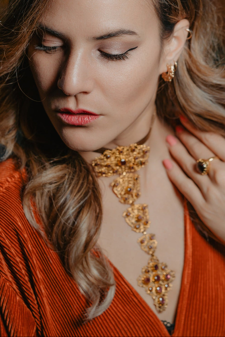Woman wearing a gold necklace and orange top with a blurred background