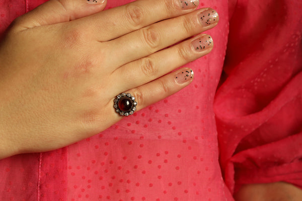 Hand wearing a ring with a red gemstone against a pink background