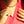 Person wearing a red shirt with a gold necklace and a ring with a red gemstone.