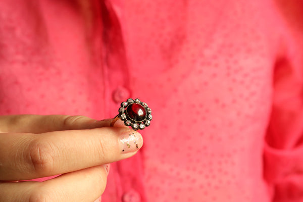 Hand holding a ring with a red gemstone against a pink background