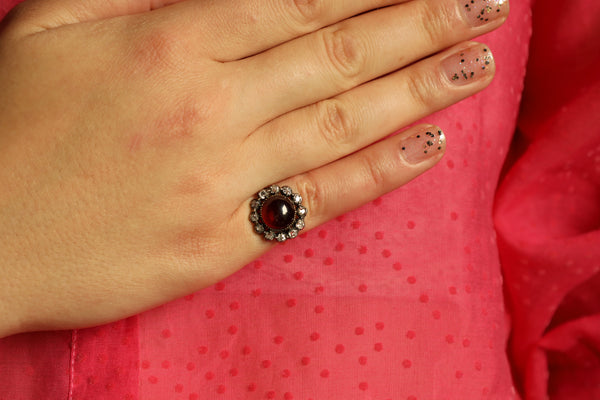 Hand wearing a ring with a red gemstone on a pink fabric background