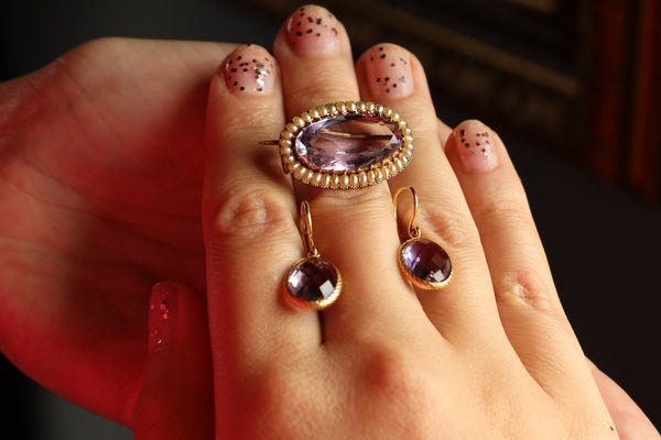 Close-up of a hand wearing a gold ring with purple gemstone on a dark background