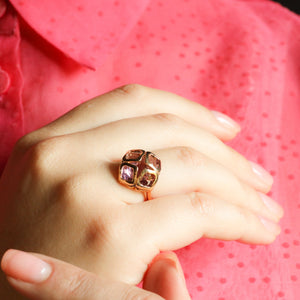 Hand wearing a gold ring with pink gemstones against a red shirt background