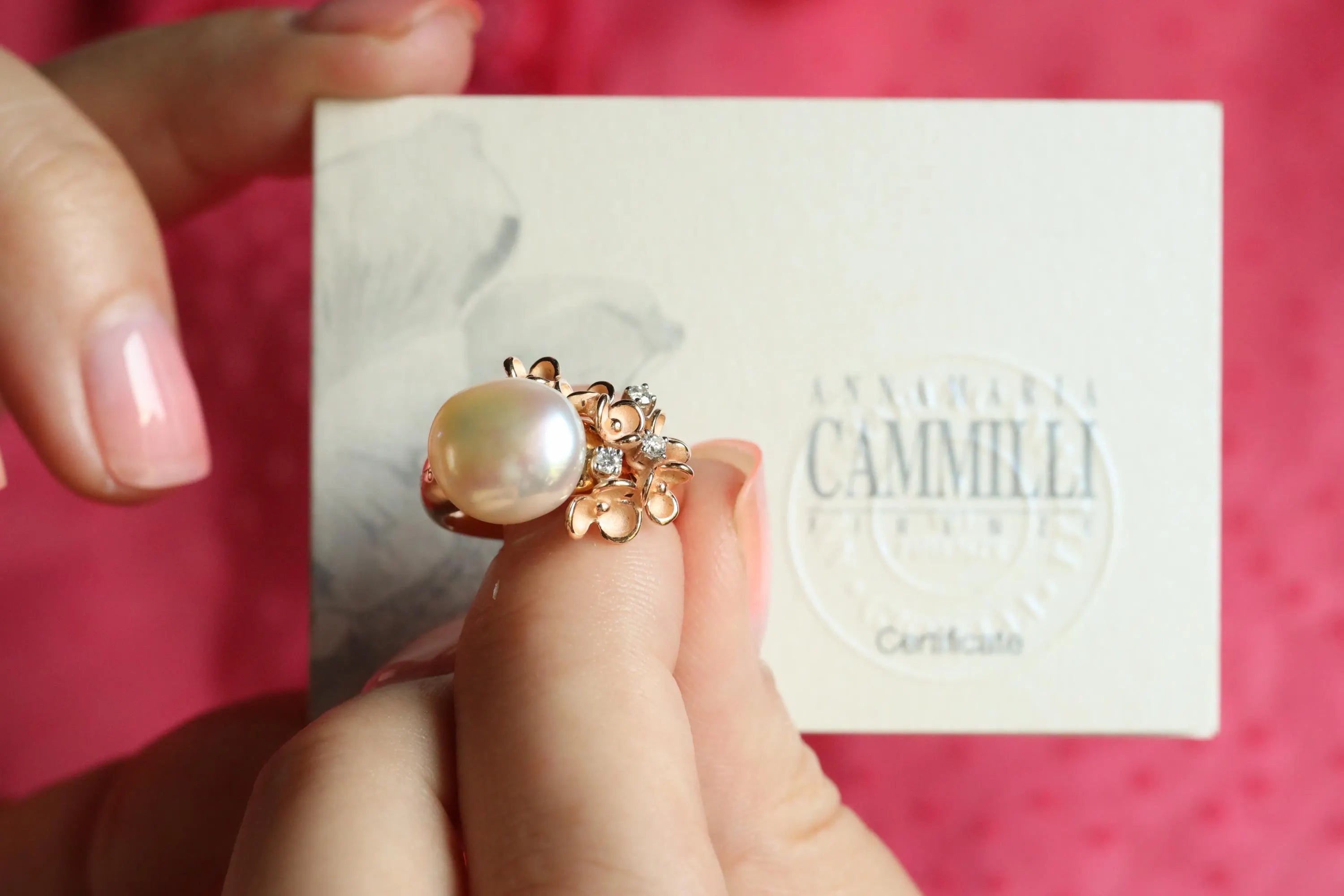 Pearl earring held by a hand on a pink background with 'Camille' branding.