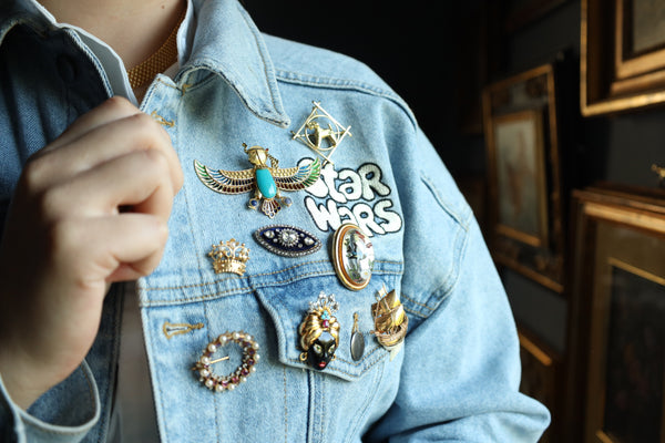 Person wearing a denim jacket with various pins, including a 'Star Wars' pin, in an indoor setting.