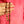 Hand holding a decorative gold and red beaded necklace against a pink background