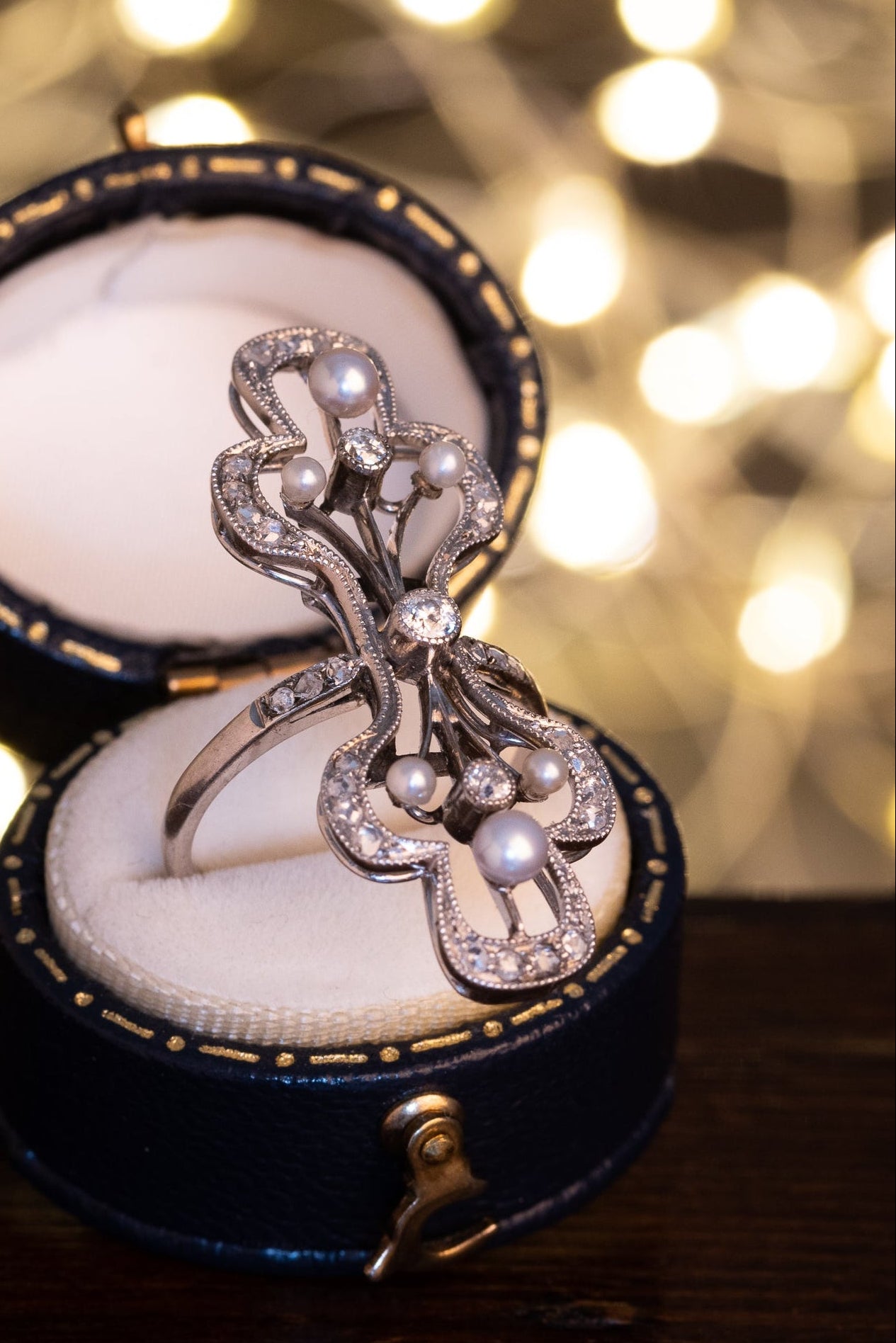 Elegant Edwardian Era ring with diamonds in a jewelry box against a blurred festive background