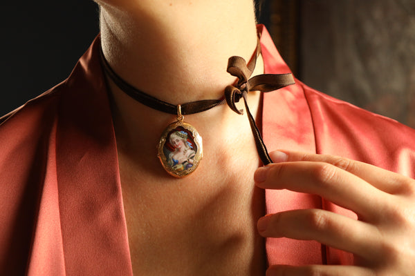 Necklace with a pendant featuring a portrait, worn by a person in a red garment.