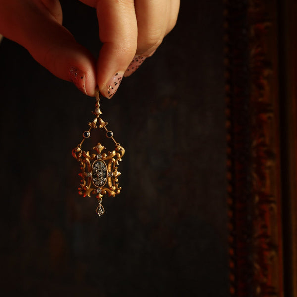 Close-up of a hand holding an ornate gold pendant against a dark background