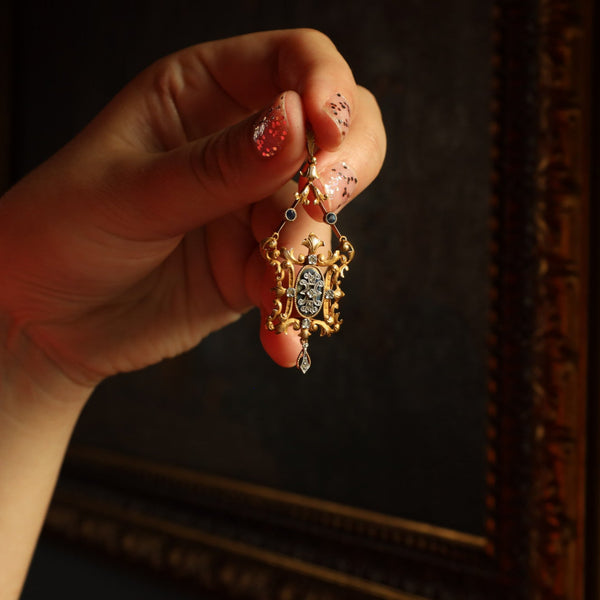 Hand holding a gold pendant with intricate design against a dark background