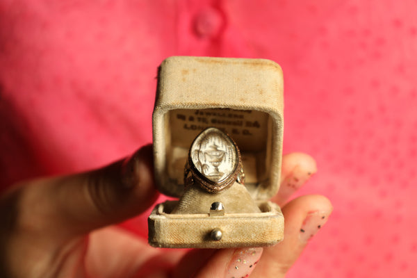 Vintage ring in a small box held by a hand against a pink background