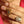 Close-up of a hand wearing a gold ring with a pendant, against a pink background.