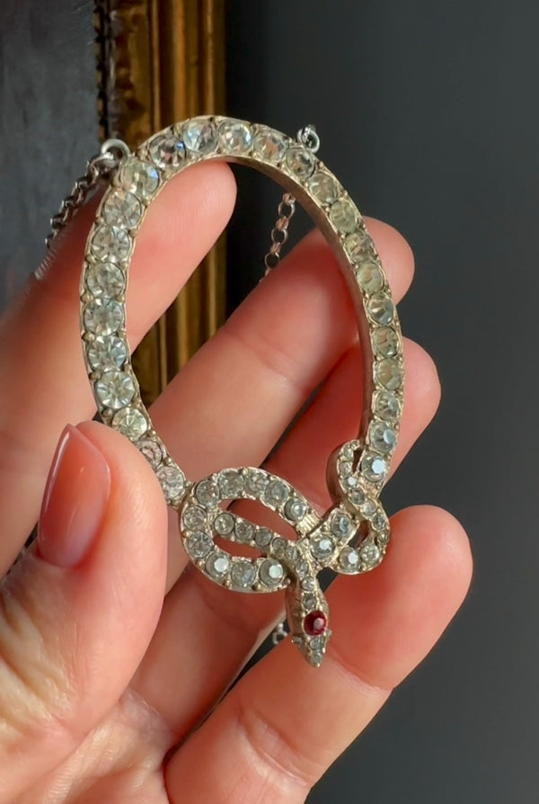 Silver snake-shaped pendant with gemstones held in a hand against a dark background