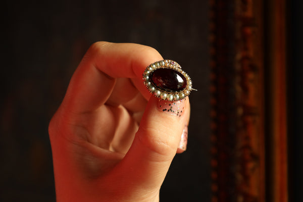 Hand holding a ring with a dark stone against a dark background
