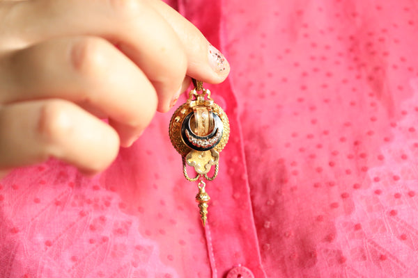 Gold key-shaped pendant held by a hand against a pink background