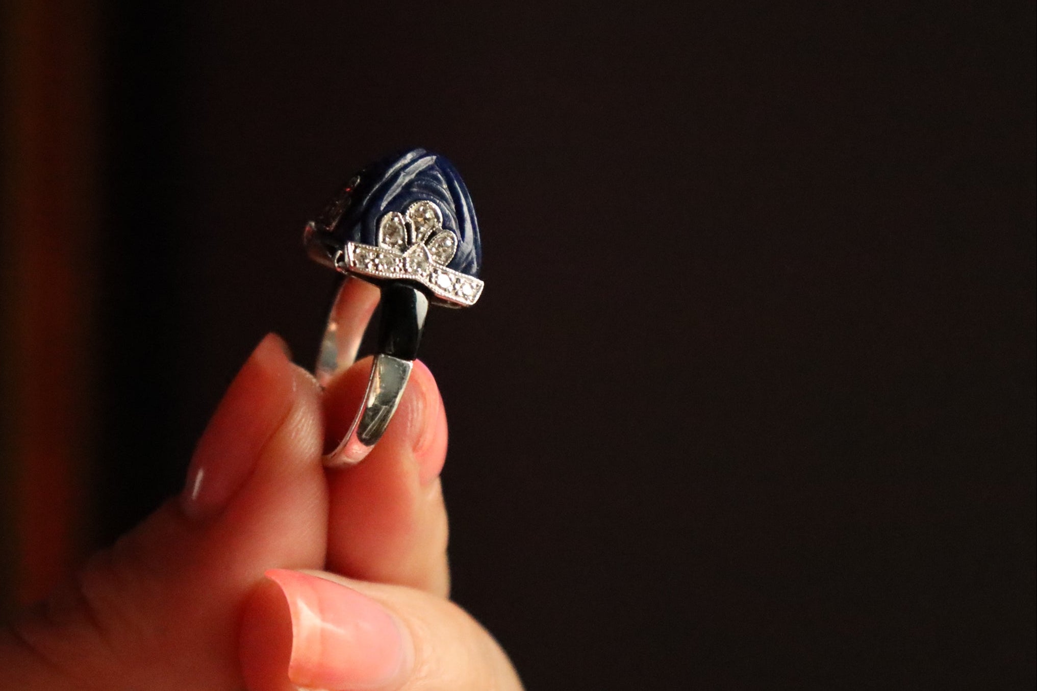 Hand holding an onyx ring with intricate design against a dark background
