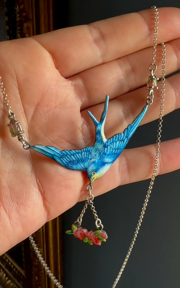 Blue bird-shaped pendant on a chain held in a hand against a dark background