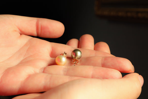 Two pearl earrings held between fingers against a dark background