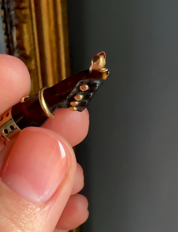 Close-up of a hand holding a small decorative object with gold and black details against a dark background.