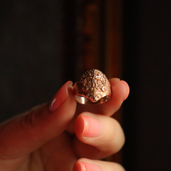 Rose gold ring held between fingers against a dark background