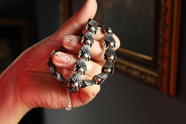 Hand holding a silver bracelet with shell-like design against a dark background