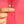 Gold pearl earrings held by a hand against a pink background