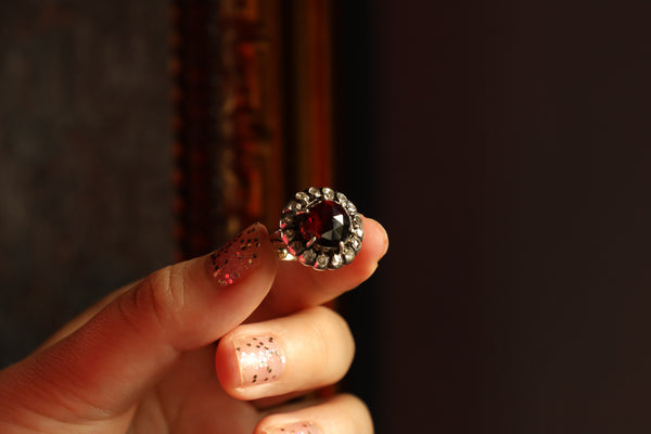 Hand holding a ring with a red gemstone against a dark background