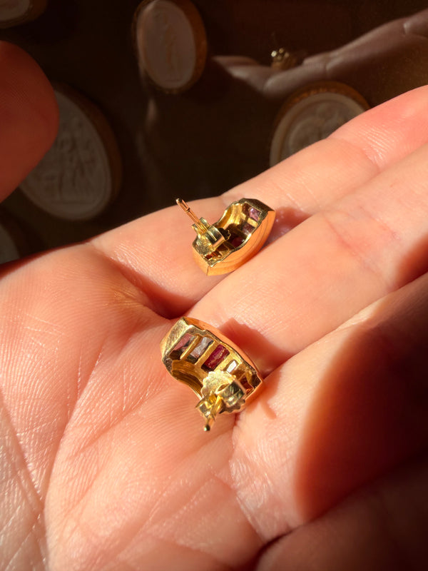 Gold earrings with gemstones held in a hand against a blurred background