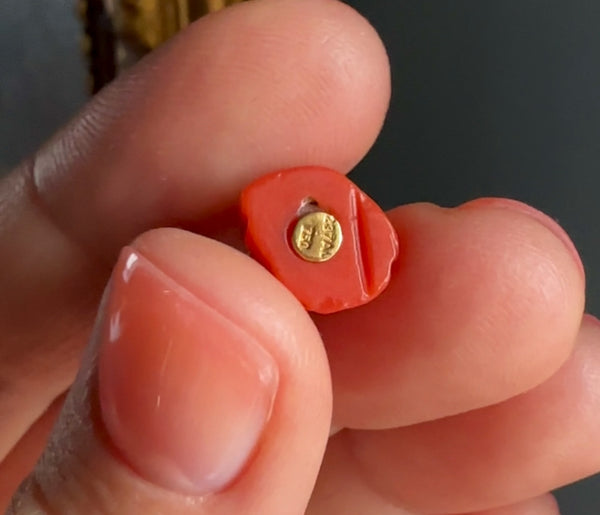 Small red heart-shaped object with a gold emblem held between fingers against a dark background