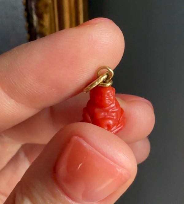 Red coral pendant with gold chain held between fingers against a dark background