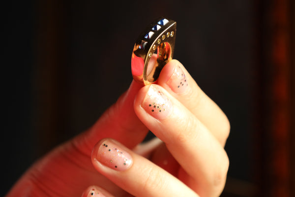 Hand holding a decorative ring with intricate design against a dark background