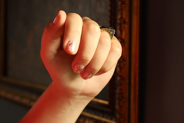Close-up of a hand with painted nails holding a small object against a blurred background