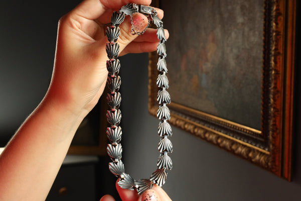 Hand holding a silver necklace in front of a dark wall with a framed picture.