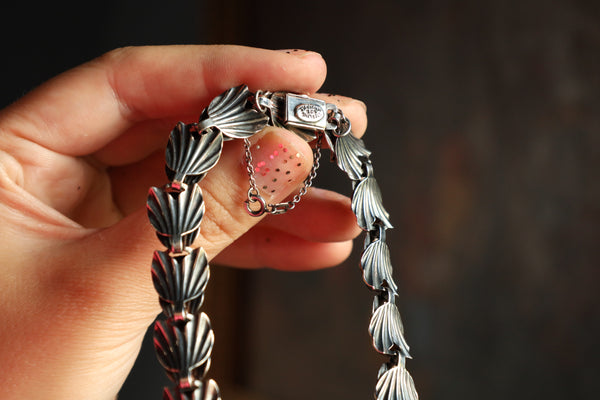 Hand holding a silver bracelet with intricate designs against a dark background