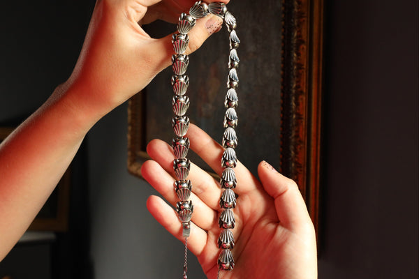 Person holding a silver necklace with intricate designs against a dark background