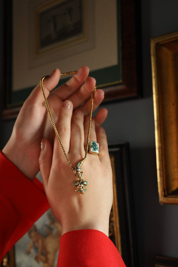Person holding a gold necklace with a green pendant in front of a mirror.