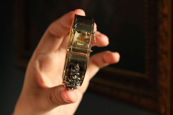 Hand holding a gold bracelet with a dark background