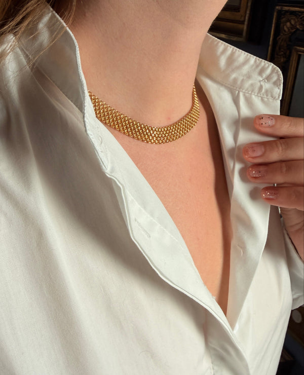A close-up of a person wearing a delicate gold chain necklace, with their white shirt open to display the jewelry.