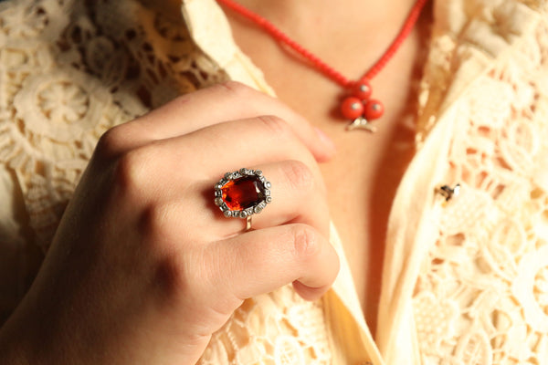 Close-up of a hand wearing a red gemstone ring with a blurred background