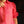 Person wearing a red blouse holding an orange beaded necklace against a dark background